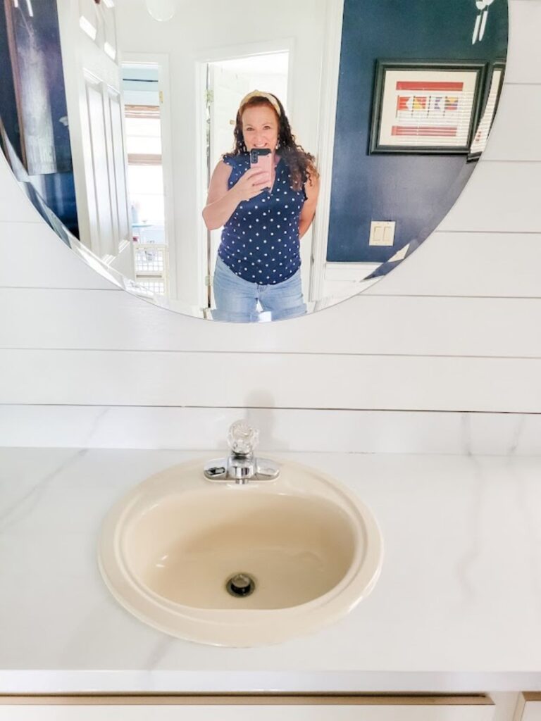 woman with phone in front of mirror and white marble bathroom vanity countertop