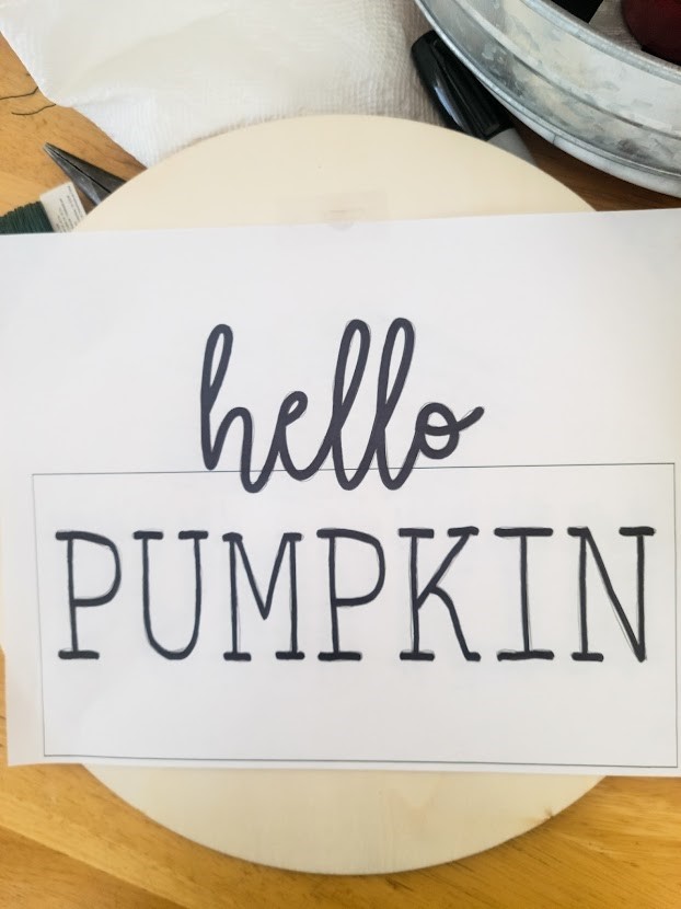 tracing "hello pumpkin" onto the wood disc