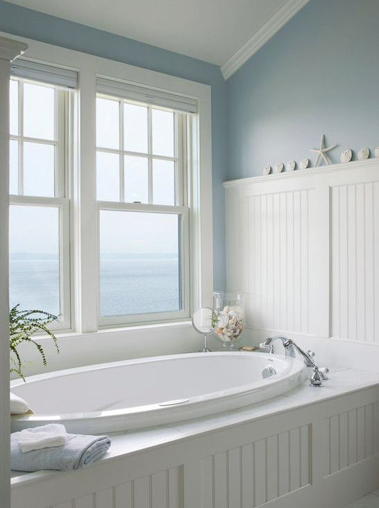 bath tub with white wainscoting and large window