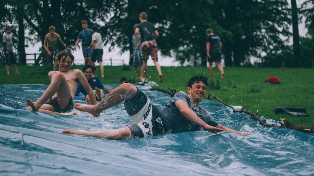adults sliding on a water slip n slide