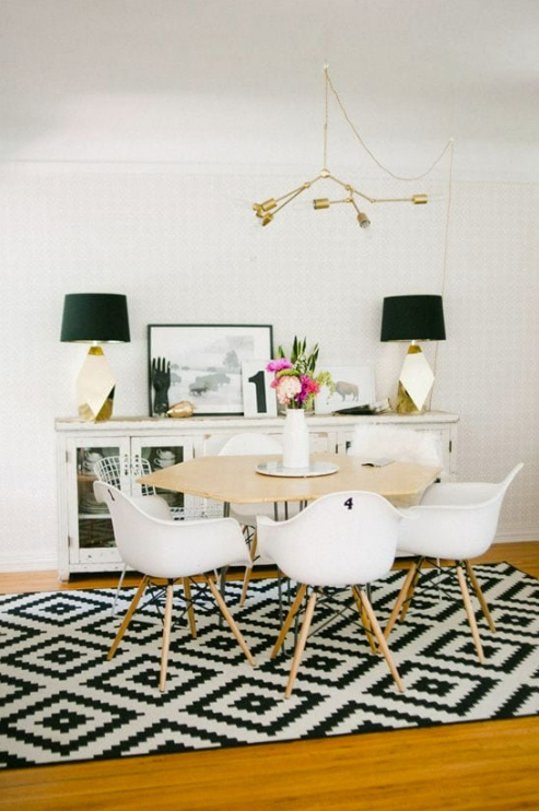 white dining room with large geometric black and white rug and brass chandelier