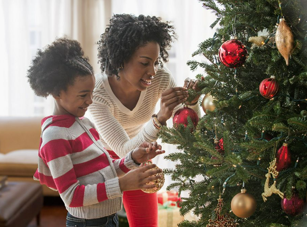 a woman and a child decorating a Christmas tree