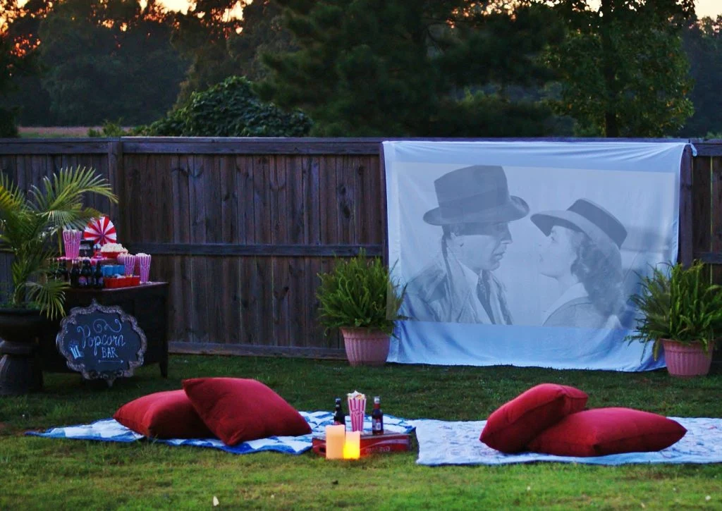 outdoor movie on a white sheet with a blanket and pillows on the ground