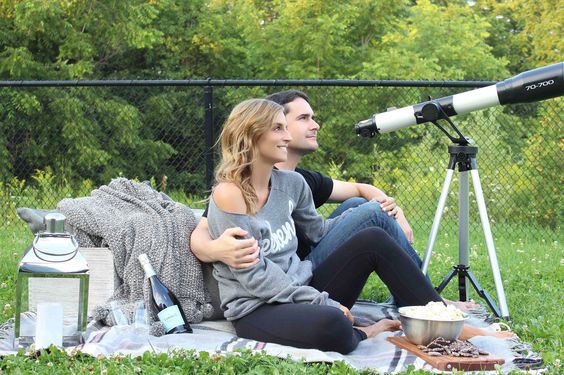 man and woman sitting on the ground in front of a telescope