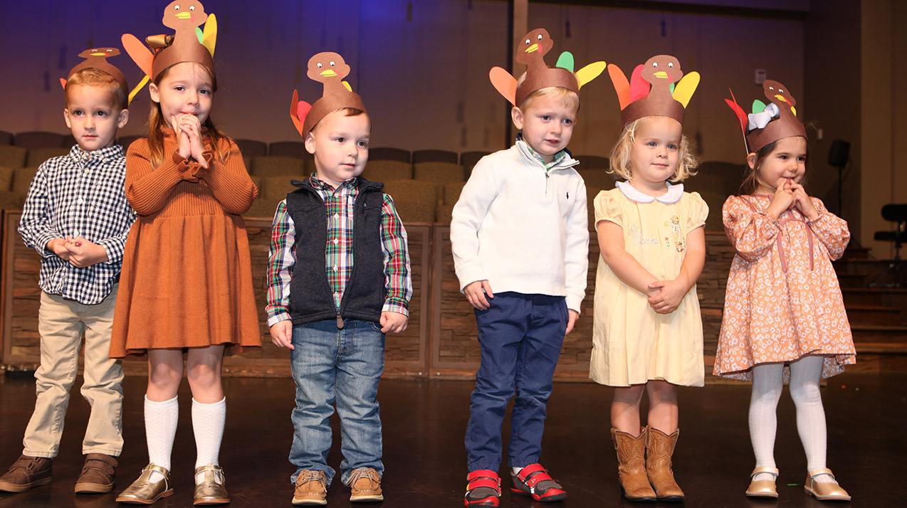 children on a stage with construction paper turkey hats