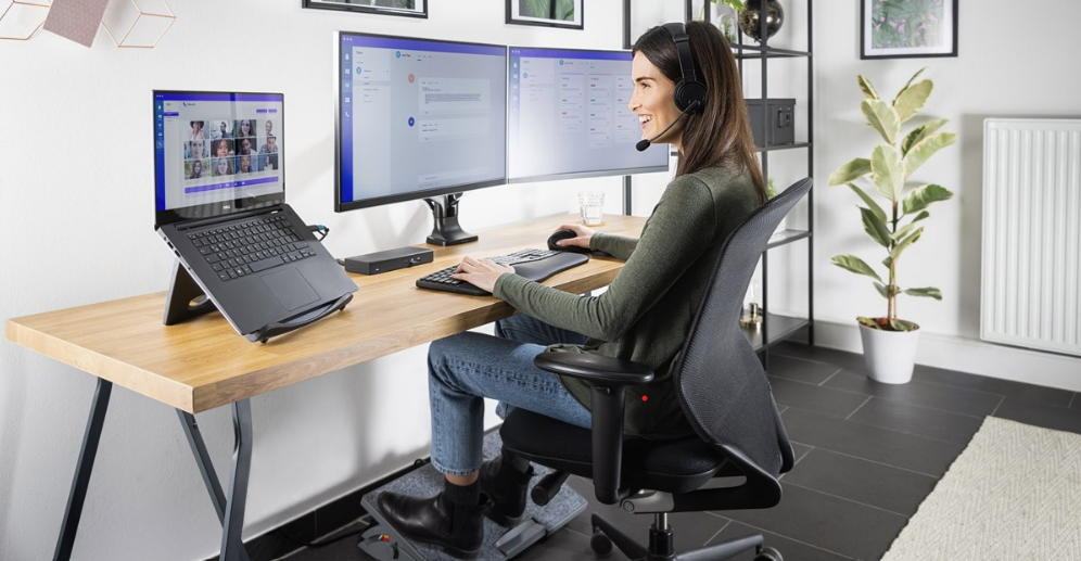 woman wearing a headset and sitting in front of a laptop with triple screens.