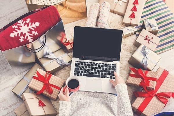woman shopping online on a laptop with wrapped presents all around