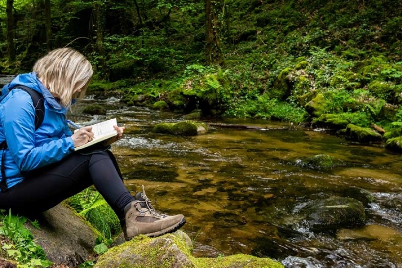 girl sitting by a stream writing in a journal