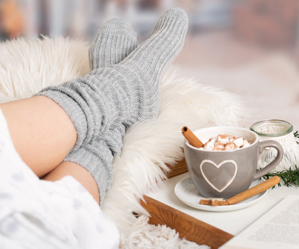 A pair of feet with socks on a furry blanket and a cup of hot chocolate