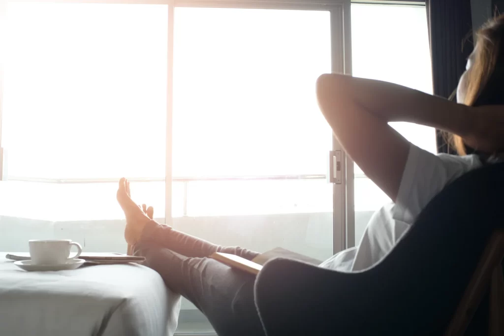 person with their feet up on a footstool relaxing in front of a large window