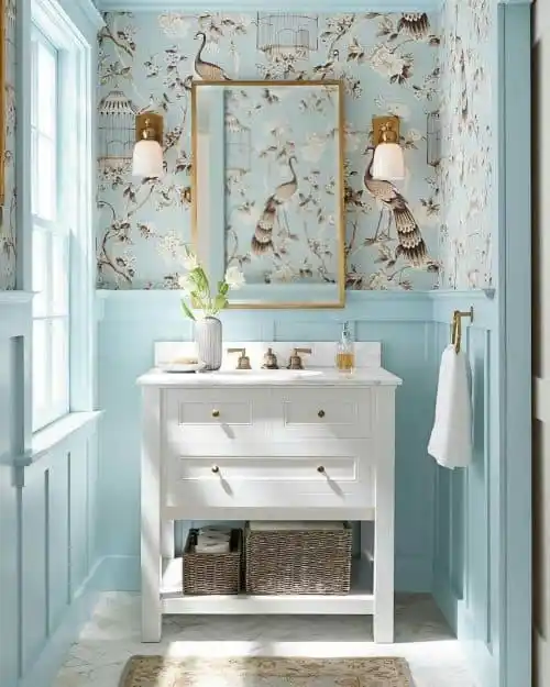 A bathroom with a white vanity, blue wainscotting, and busy wallpaper