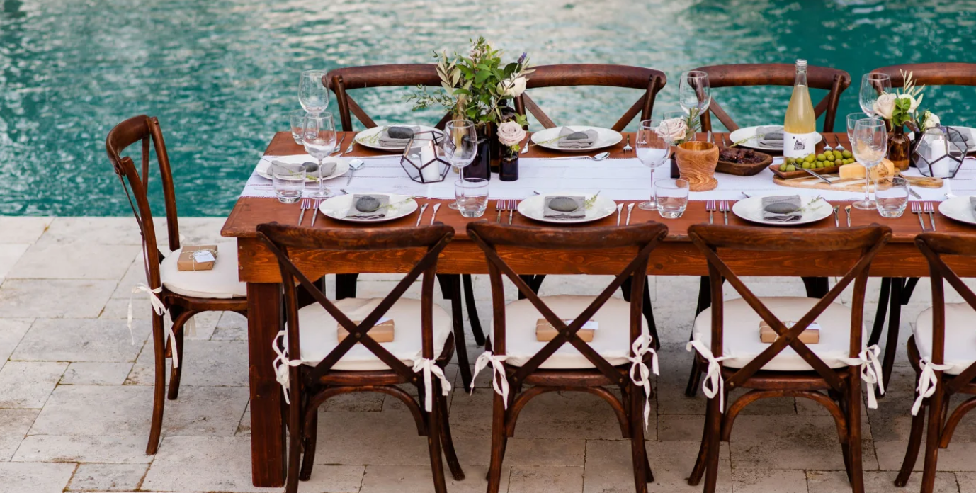 dinner table set by a pool hosting an outdoor party
