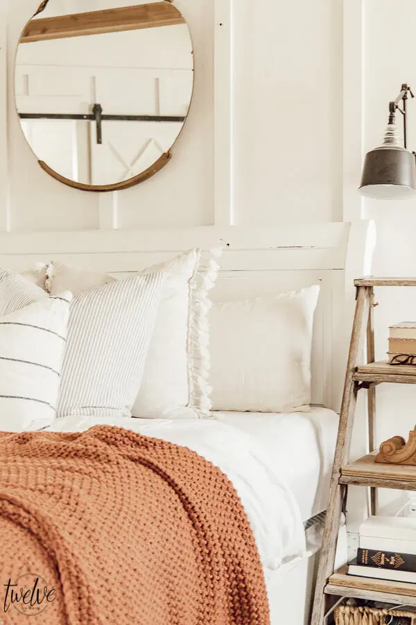 white bedroom with an orange blanket and a ladder as a side table minimalist fall decor ideas