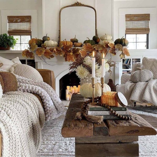 white living room with a fireplace decorated with fall greenery and chunky knitted blankets