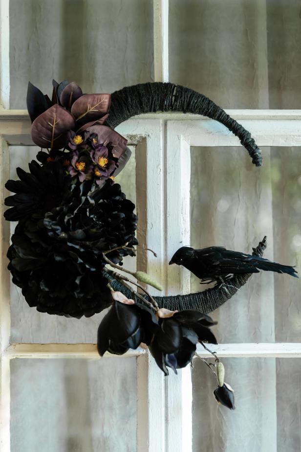 a black crescent moon shaped wreath with black flowers and a crow upscale halloween home decor