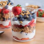 a clear glass filled with berry and granola parfait