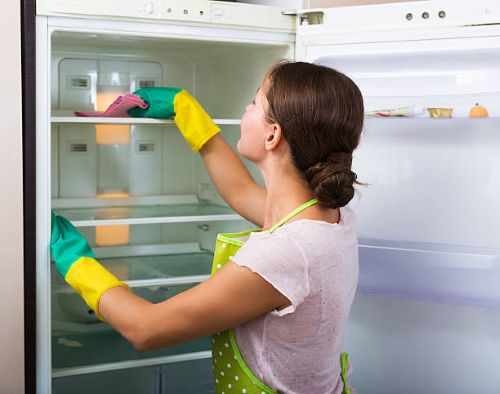 a woman cleaning out the refrigerator how to have a clean home all summer
