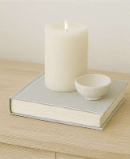 a white cylinder candle sitting on a grey book with a small white bowl beside how to add a relaxing summertime vibe to your home