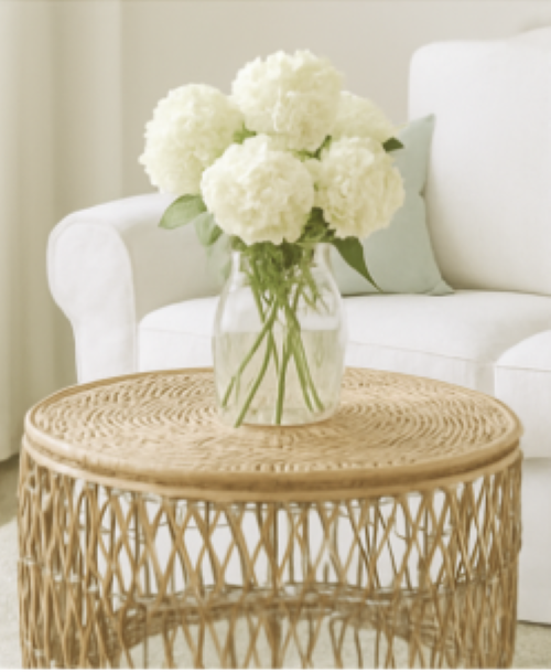 A bouquet of white hydrangea in a clear glass vase sitting on a rattan coffee table how to add a relaxing summertime vibe to your home