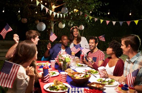 4th-of-July-backyard-party-Inspireme2diy people sitting at an outdoor table eating with American flags fun 4th of July activities