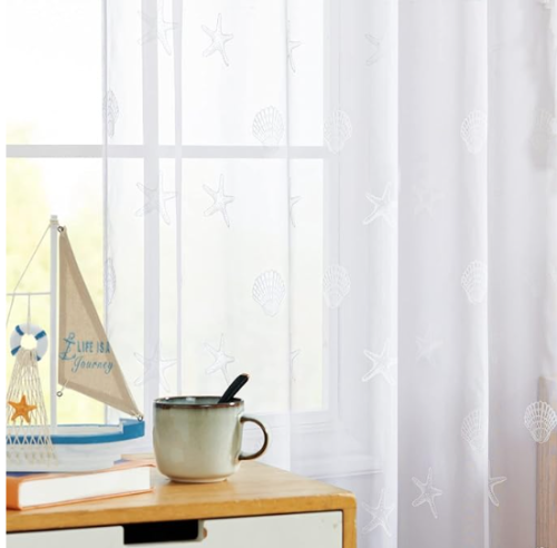 a table with a sailboat and coffee cup in front of white curtains