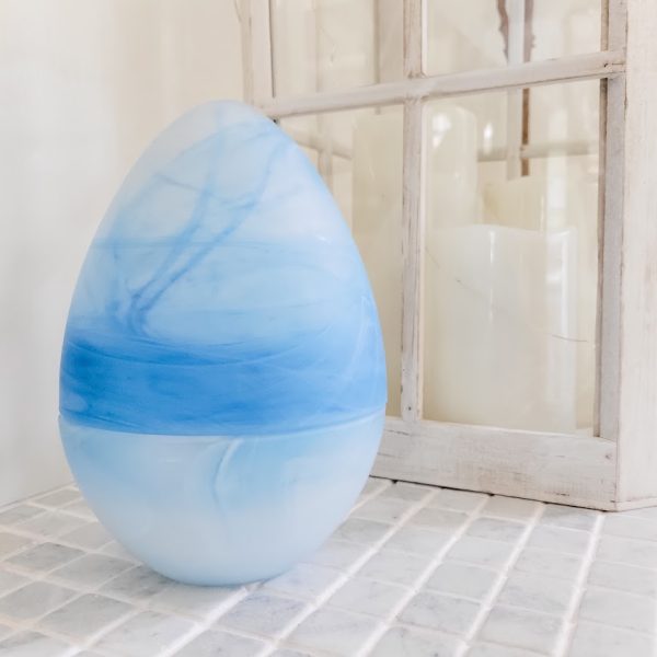 blue glass egg on a tile surface next to a white lantern