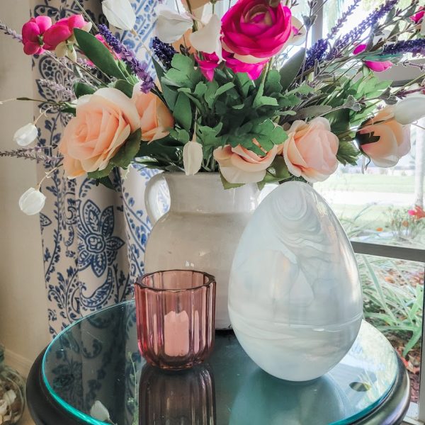 white glass egg on a table next to a vase of flowers