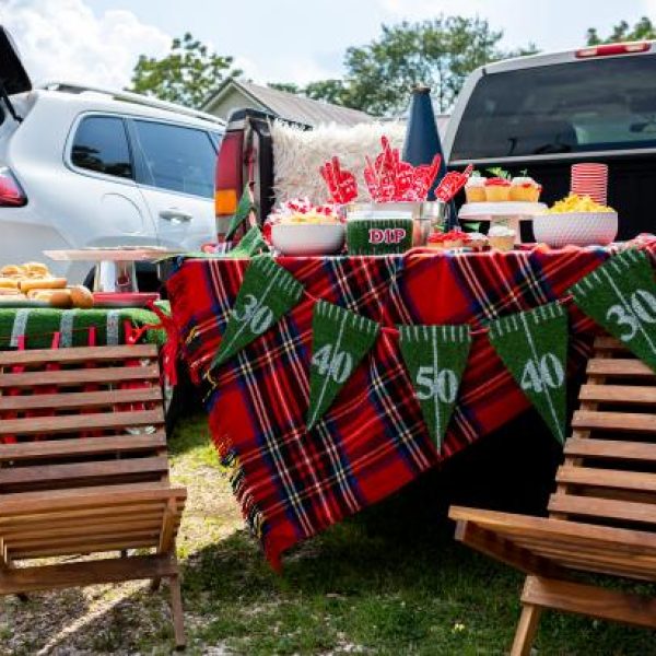 two outdoor chairs with table covered with a red plaid tablecloth and turf yard marker garland