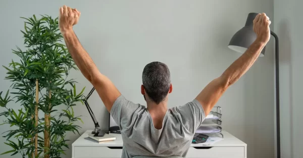 person sitting in a chair with his back to the camera stretching with both arms in the air 10 relaxing tips to reduce stress in your home