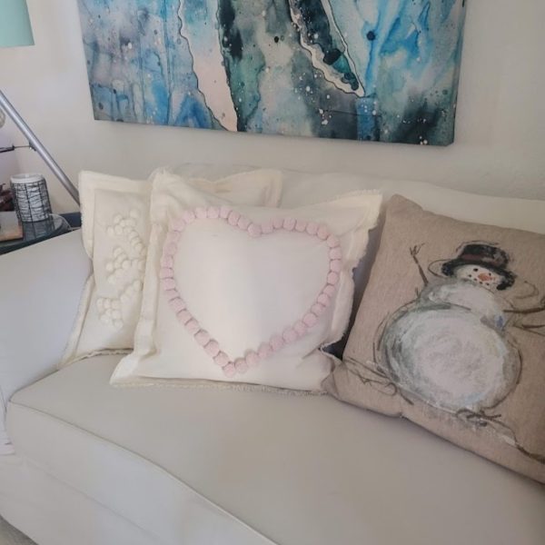 A picture containing both the snowflake and the heart pompom pillows along with my store bought snowman pillow on my white slipcovered sofa.