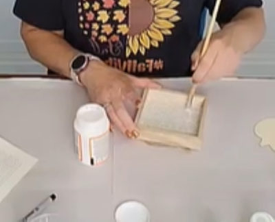 a woman painting a small wooden frame