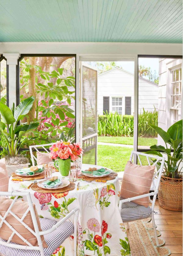 outdoor dining table on a screened porch with colorful flowers in a green vase