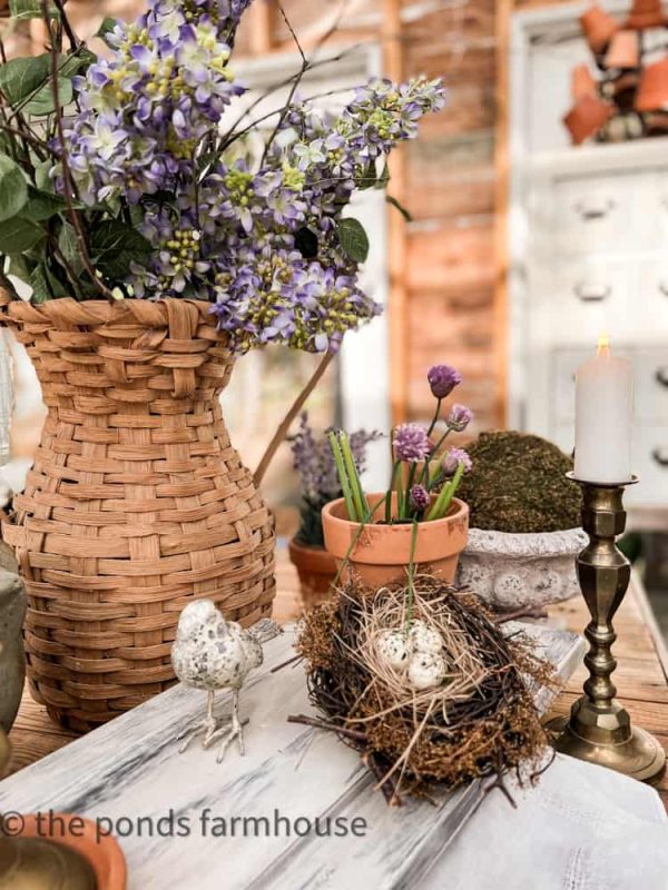 large basket of flowers on a table with a bird's nest and terracotta pot