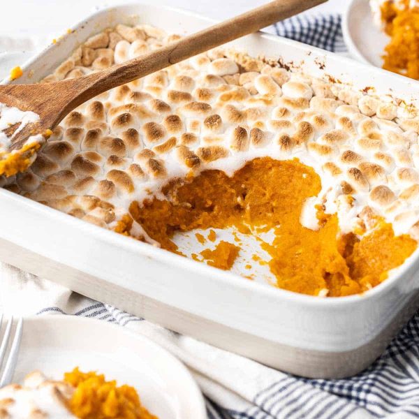 a white rectangle casserole dish sitting on a table with sweet potatoes and a marshmallow topping great fall side dishes