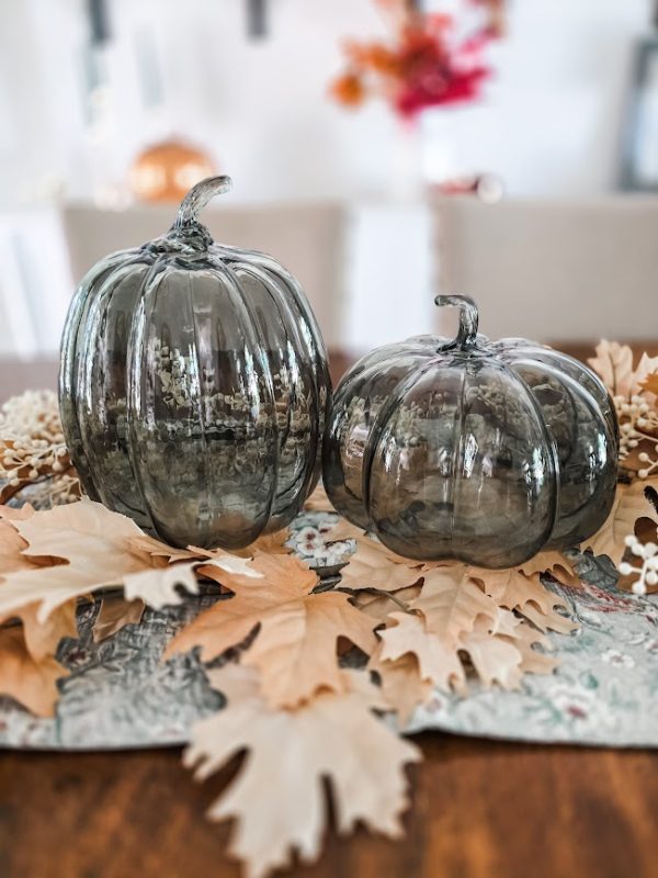 2 green glass pumpkins sitting on fall florals on a table