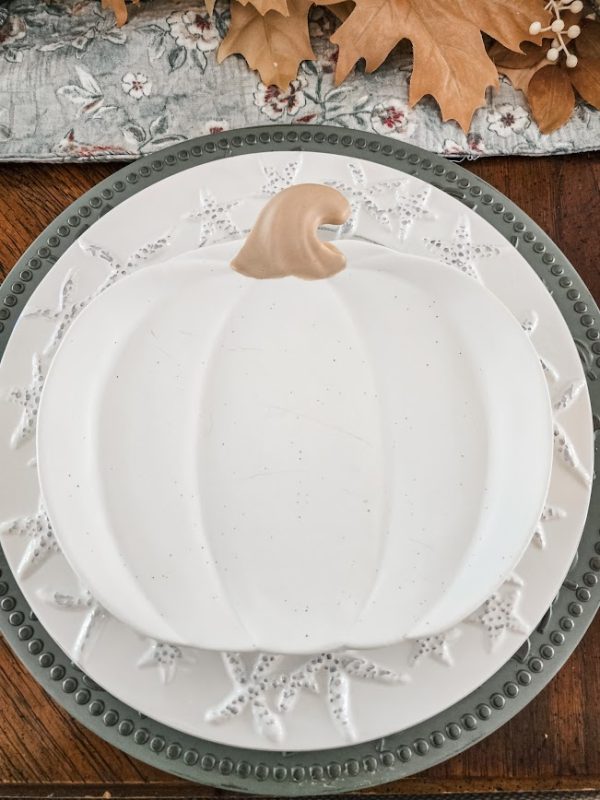 a green charger with a white seashell-embossed dinner plate and a pumpkin-shaped plate on the top crafting the perfect tablescape