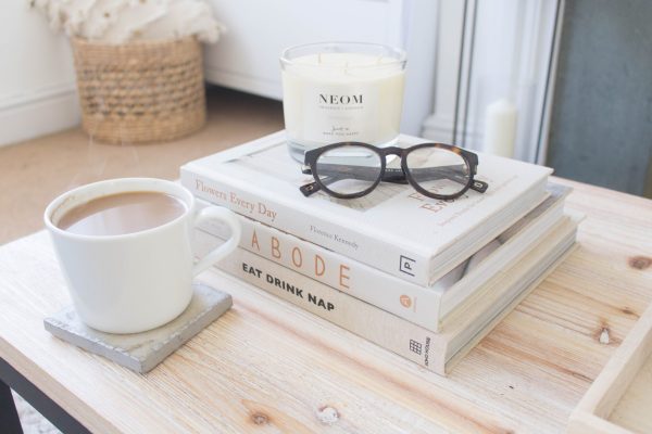a stack of white books on a wood table and a cup of coffee