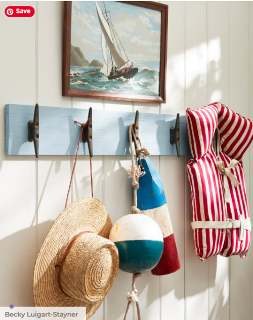 A coastal blue coat rack and a shiplap wall with buoys, a straw hat and a life jacket hanging from it going coastal for under $100