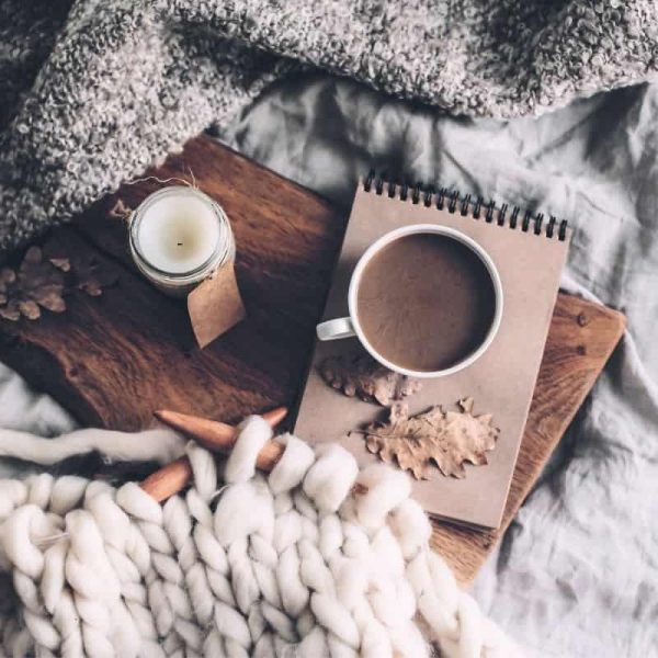 unfinished knitting sitting beside a cup of cocoa and a candle