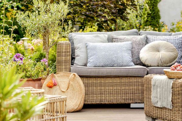 A patio with wicker furniture and grey cushions