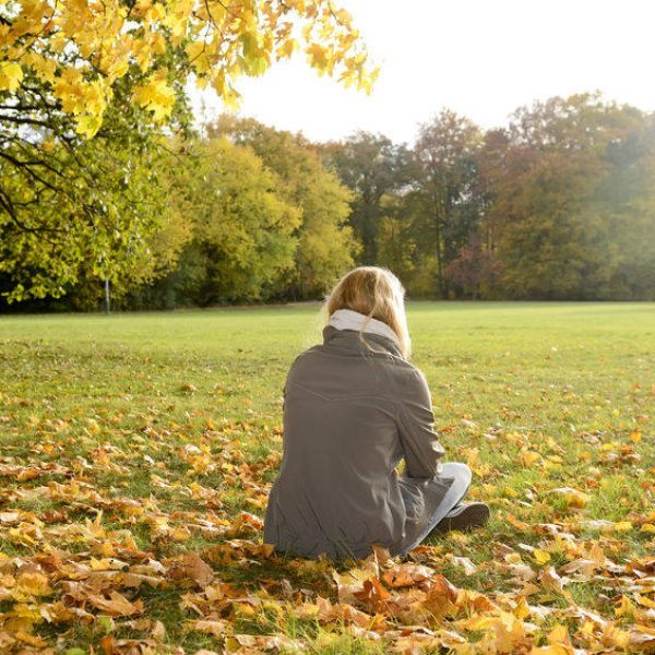 girl sitting in the grass with autumn leaves