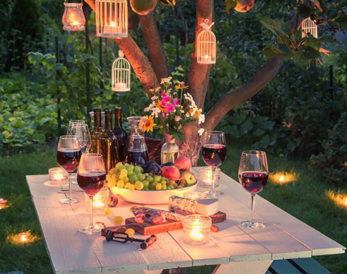 outdoor party with hanging lighted birdcages in the trees and red wine in glasses planning the perfect spring garden party
