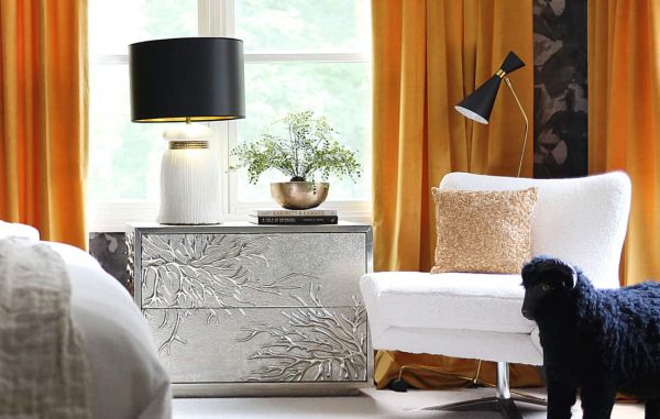 White chair with a textured pillow and orange velvet drapes