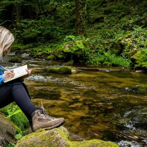 girl sitting by a stream writing in a journal