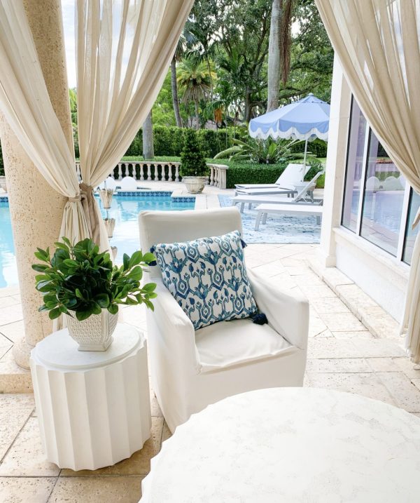 a white slipcovered chair with a blue pillow on a patio by a pool patio decor ideas