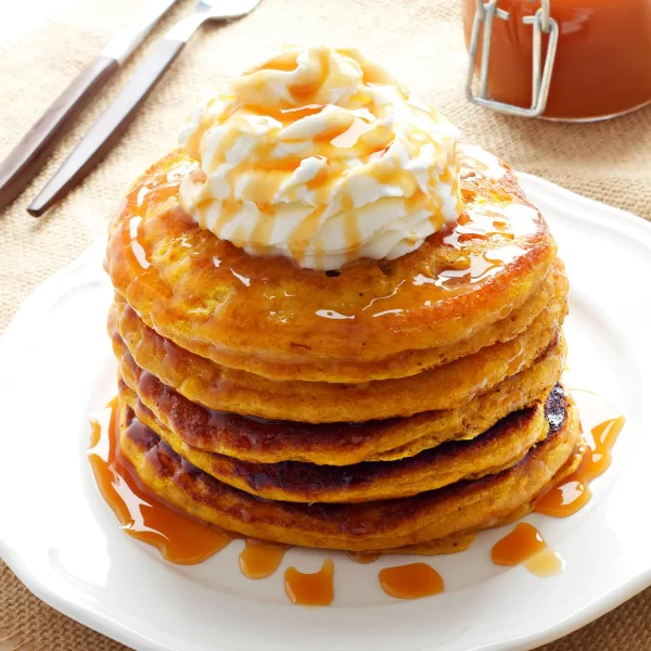 stack of pancakes with whipped cream and syrup