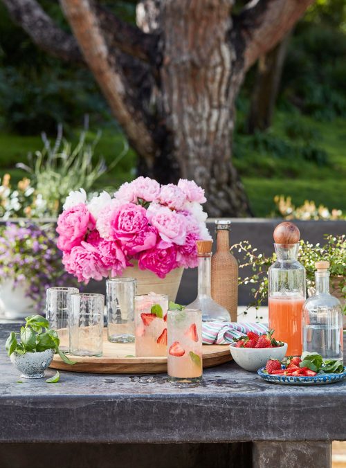 an outdoor table set with a bouquet of peonies, plates, and drinks with strawberries planning the perfect spring garden party