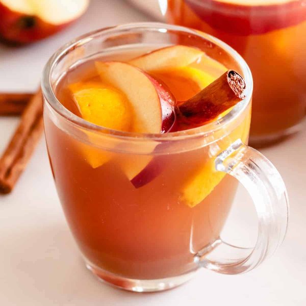 hot apple cider in a mug with sliced apples and a cinnamon stick