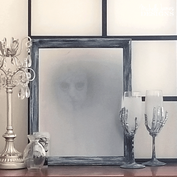 A mirror with a spooky face in it, silver candlesticks and skeleton hand stemmed wine glasses on a table