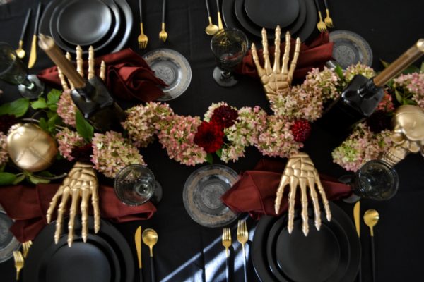 a black and burgundy spooky tablescape with skeleton hands at each place setting